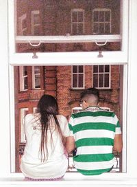 Rear view of women sitting on window