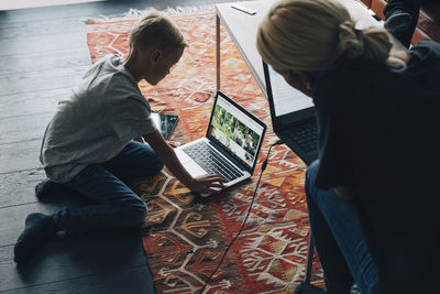 High angle view of woman looking at boy using laptop by coffee table in living room at home