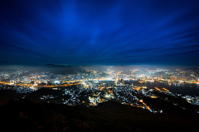 Aerial view of illuminated city against dramatic sky at night