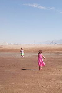 Girl playing on sand in desert against clear sky
