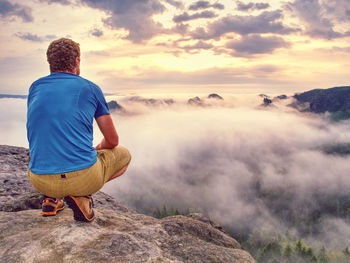 Person on a top of mountains in a misty cloud.  tourist sits on his heels and watches the sunrise