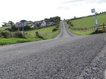 Country road amidst field against sky