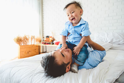 Cheerful father playing with son on bed at home