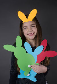 Portrait of smiling girl with eater bunny and pom pom in basket against gray background