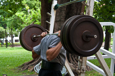 Midsection of man lifting barbell on field
