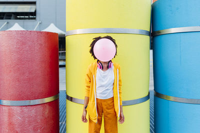 Young woman blowing bubblegum in front of colorful pipes