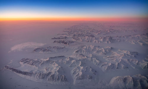 Aerial view of snowcapped landscape against sky during sunset