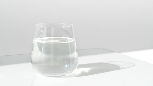 Glass of fresh water on white background with sunlight and deep shadow of glass.