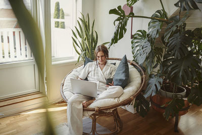 Woman sitting in papasan chair and using laptop