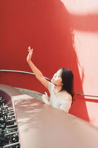 High angle view of young woman standing at railing against red wall