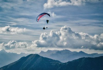 People paragliding above mountains against cloudy sky