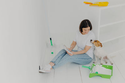 Woman with dog sitting on floor against wall at home