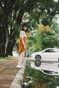 Full length portrait of woman standing on sidewalk by puddle