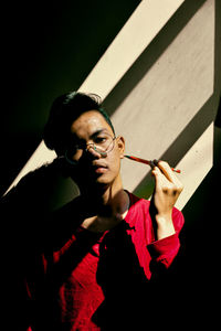 Portrait of young man holding pen while standing against wall