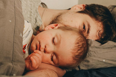 Portrait of father sleeping with baby on bed at home