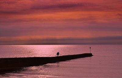 Silhouette person on sea against sky during sunset