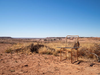 Scenic view of .ry arid landscape against clear blue sky with old seat frame in foreground