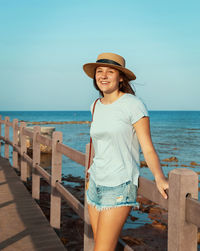 Portrait of beautiful young woman standing at beach against sky