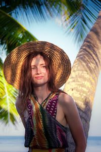 Young woman wearing hat standing by tree trunk at beach