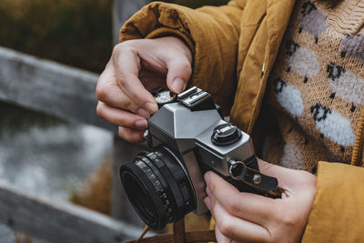 Close-up cropped photo of woman holding vintage camera, turning dial and changing settings