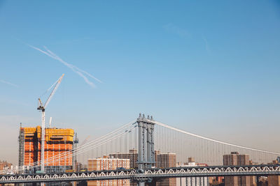 Manhattan bridge against blue sky on sunny day in city