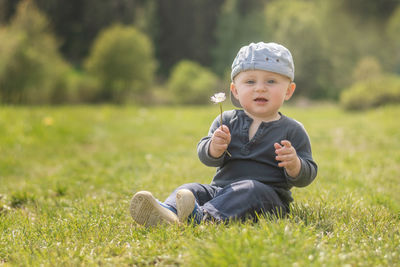 Portrait of cute baby boy sitting on grassy land in park