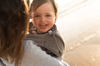 Mother carrying smiling son while standing at beach