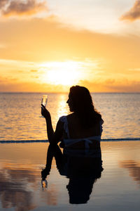 Attractive woman on a infinity pool near the ocean with a glass of champagne.back view