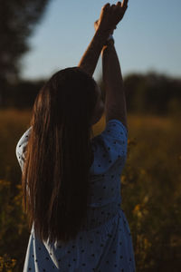 Rear view of woman with arms raised standing against sky during sunset