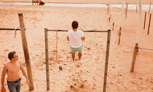 Rear view full length of man exercising on rod at beach