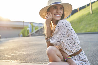 Smiling young woman wearing hat sitting outdoors