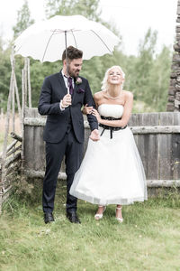 Smiling bride groom standing with umbrella on yard