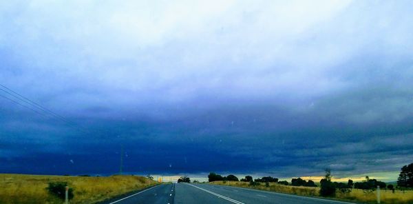 Road by landscape against storm clouds