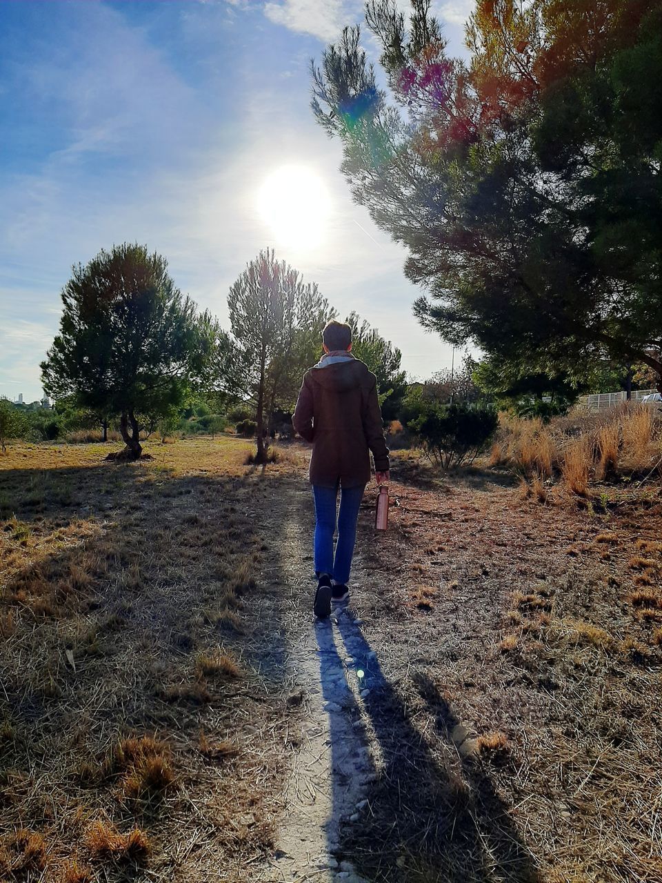 REAR VIEW OF MAN WALKING ON STREET AMIDST FIELD