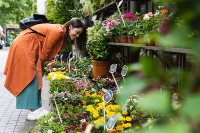 Side view of delighted female customer picking blossoming potted flowers in garden market