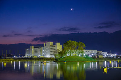 Illuminated buildings by river against sky at night