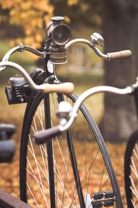 A penny-farthing bicycle with an old headlamp in a park with fallen autumn leaves