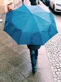 Rear view of woman holding umbrella while walking on street during monsoon