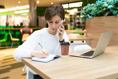 Woman taking down notes while talking on smart phone