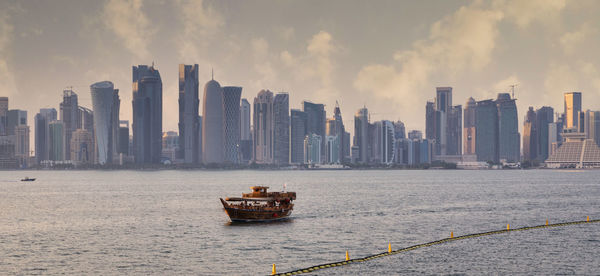 Doha skyline from the corniche promenade sunset shot showing dhow with qatar flag in the arabic gulf