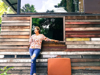 Woman looking away while standing against wooden wall