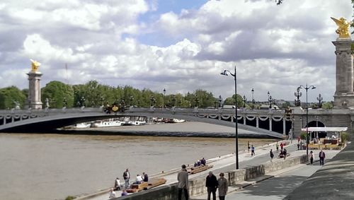 People walking on road against cloudy sky