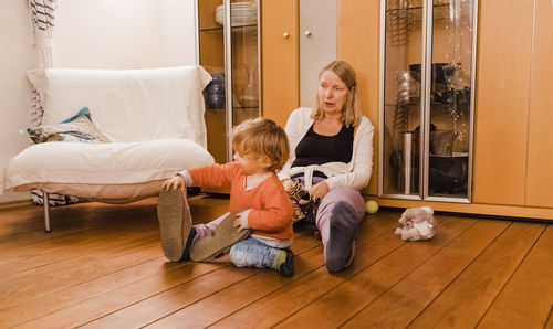 Grandmother with cute granddaughter while sitting on hardwood floor at home