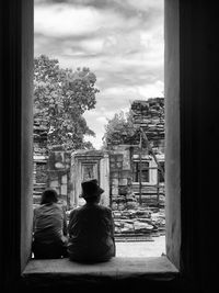 Rear view of people sitting by buildings against sky