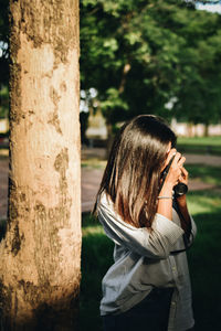 Woman photographing while standing on tree