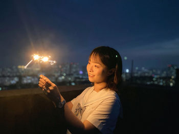 Portrait of young woman holding illuminated string lights at night