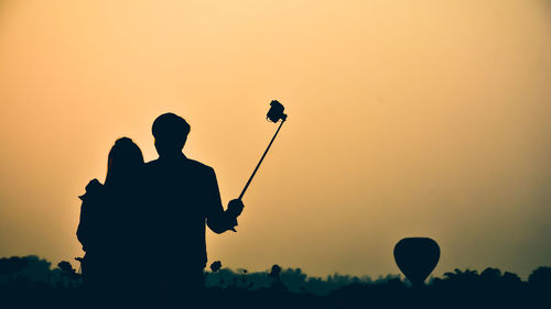 Silhouette couple taking selfie against clear sky during sunset