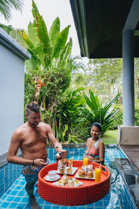 Full length of shirtless man sitting by swimming pool