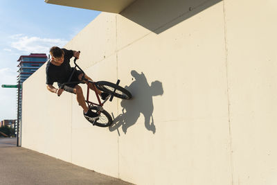 Side view of focused young male in casual clothes riding concrete wall on bmx bicycle while spending time in skate park in weekend