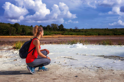 Rear view of woman sitting at beach against sky